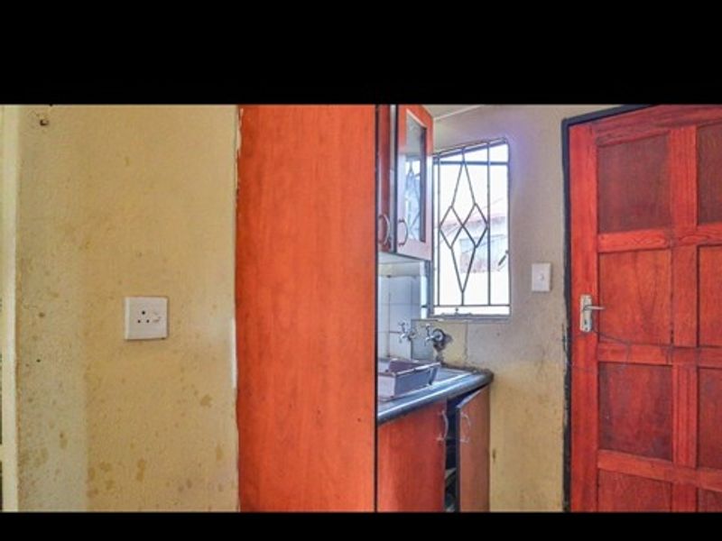 A compact kitchen area featuring built-in cabinetry and a sink, requiring cosmetic updates to the wall finishes.