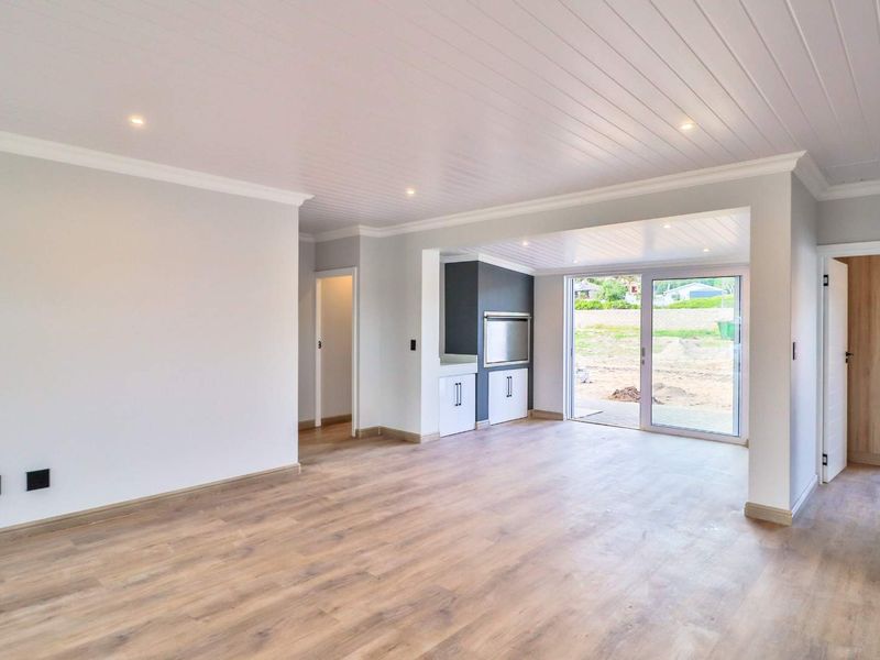 Spacious open-plan living area featuring modern laminate flooring, recessed lighting, a built-in braai, and sliding glass doors leading to the rear exterior.