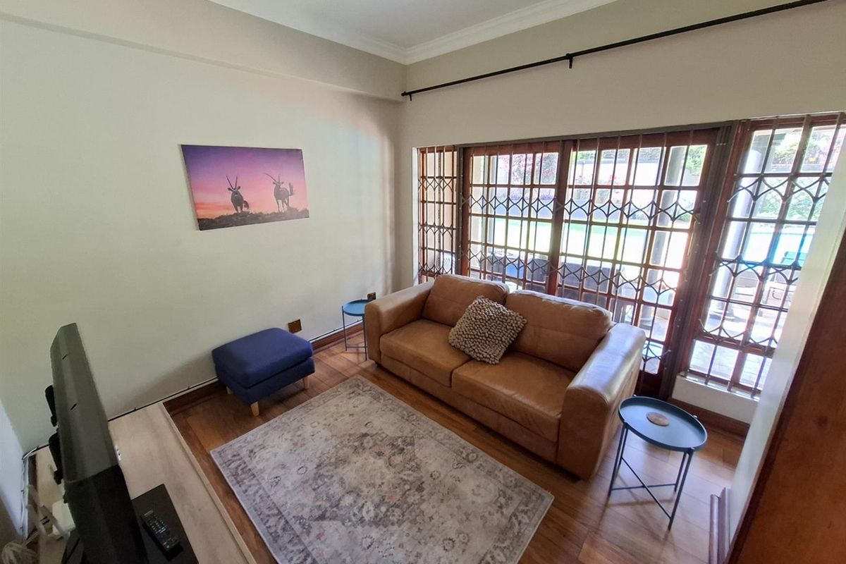 A cozy living room featuring warm wooden flooring and large glass sliding doors with security gates, providing natural light and access to the outdoors.