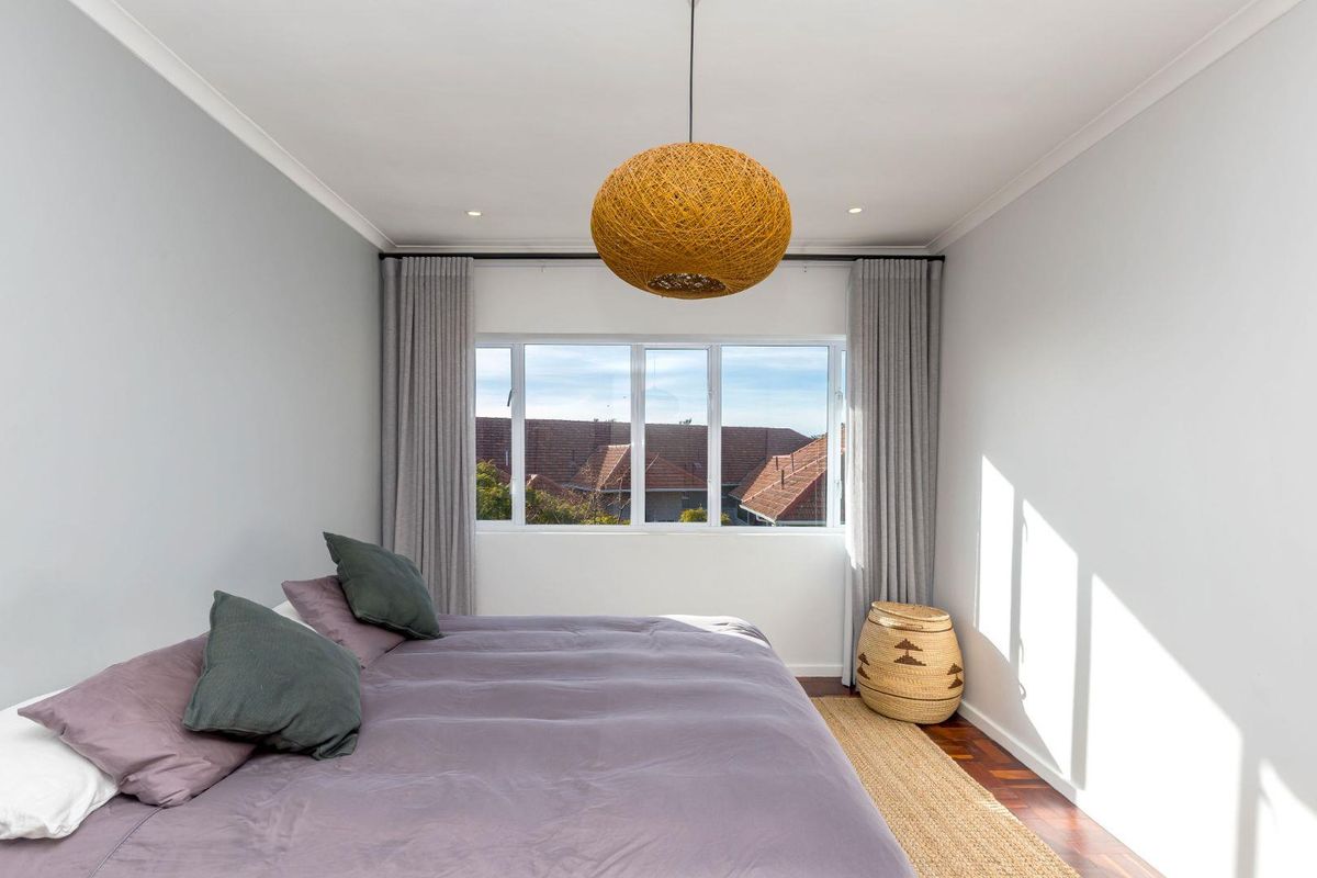 A bright and well-maintained bedroom featuring polished hardwood flooring, neutral walls, and large windows providing natural light.
