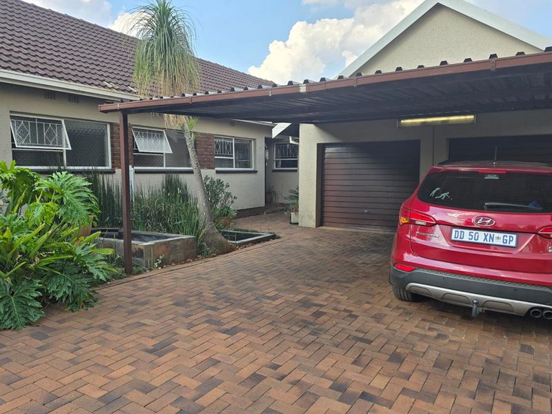 Front exterior view featuring a brick-paved driveway, a covered carport, and a secure garage entrance with established garden planters.