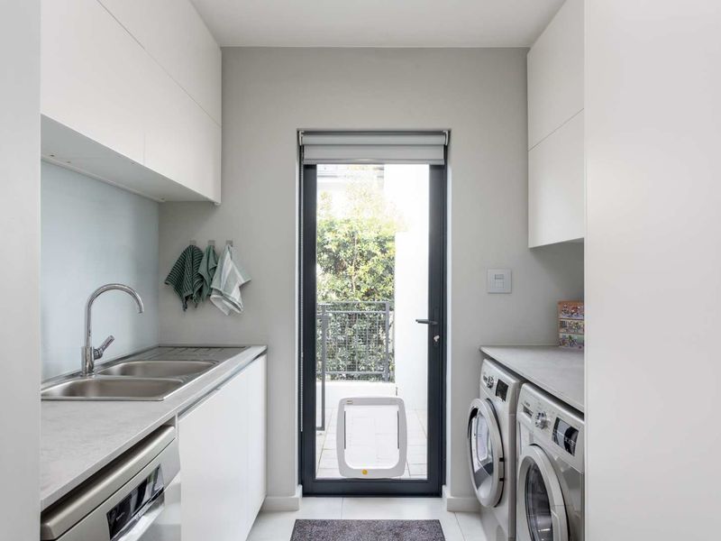 A modern, well-maintained laundry room featuring built-in cabinetry, stone countertops, a stainless steel sink, and direct access to an outdoor area.