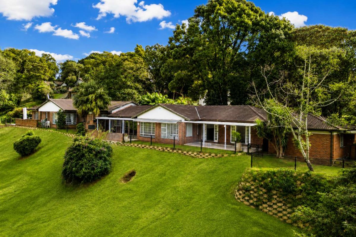 Rear view of the townhouse featuring a brick facade, tiled roof, and a covered patio overlooking a spacious, well-maintained lawn and garden area.