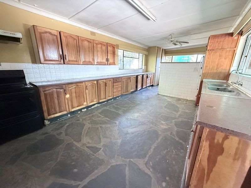 Spacious kitchen featuring wooden cabinetry, stone flooring, and a double bowl sink, offering a functional layout ready for modern renovation.