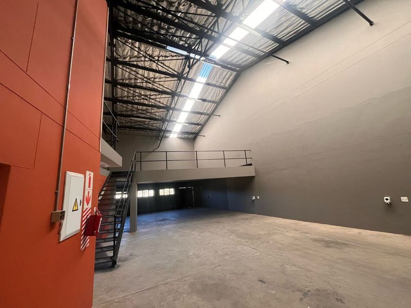 Spacious industrial warehouse unit featuring high ceilings with skylights, a mezzanine level, concrete flooring, and a metal staircase.