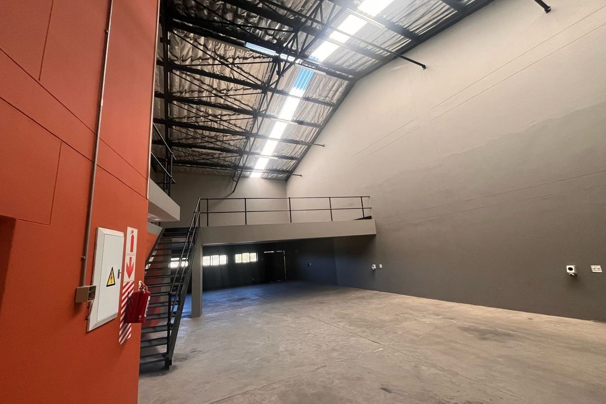 Spacious industrial warehouse unit featuring high ceilings with skylights, a mezzanine level, concrete flooring, and a metal staircase.