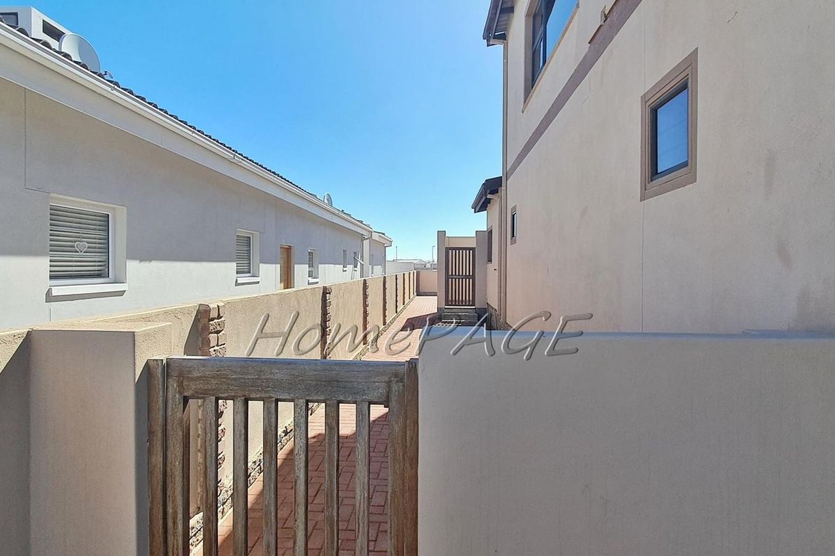 A side passage between two residential properties featuring paved walkways, boundary walls, and secure wooden access gates.