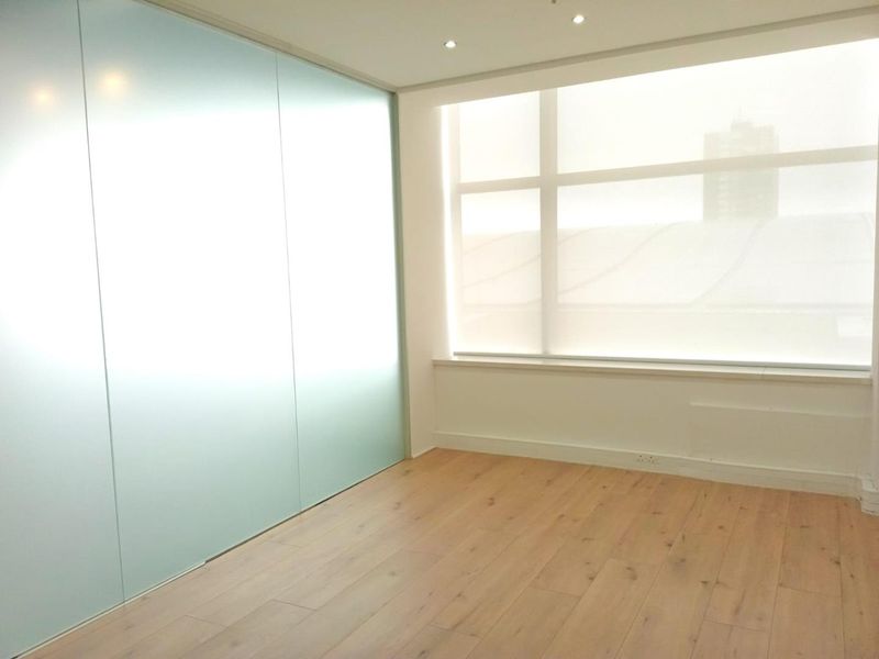 A bright, modern office space featuring timber laminate flooring, a sleek frosted glass partition, and large windows with integrated roller blinds.
