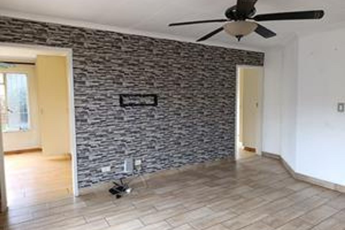 A living area featuring tiled flooring, a ceiling fan, and a decorative stone-effect feature wall with integrated electrical points.