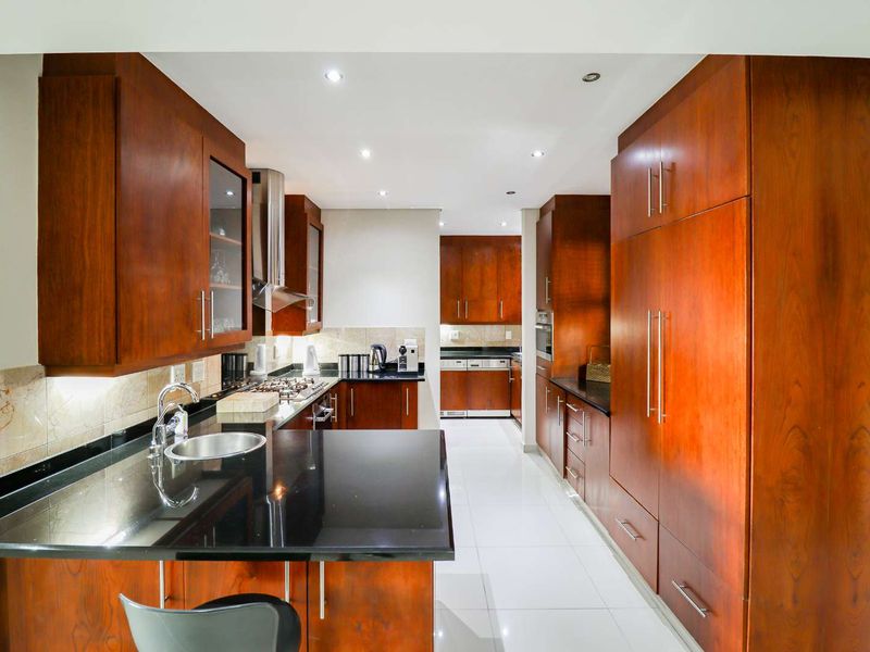 Modern kitchen featuring extensive wooden cabinetry, sleek black granite countertops, integrated appliances, and high-quality tiled flooring with recessed lighting.