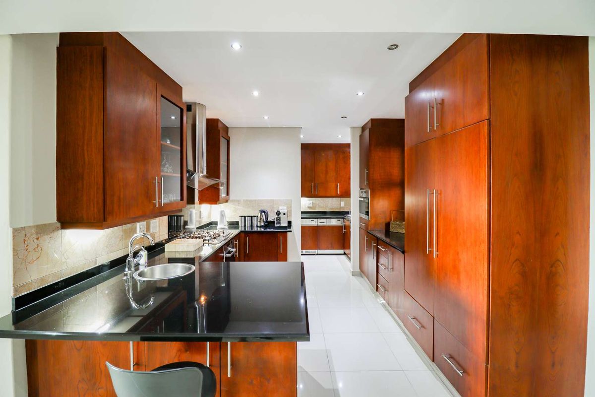 Modern kitchen featuring extensive wooden cabinetry, sleek black granite countertops, integrated appliances, and high-quality tiled flooring with recessed lighting.