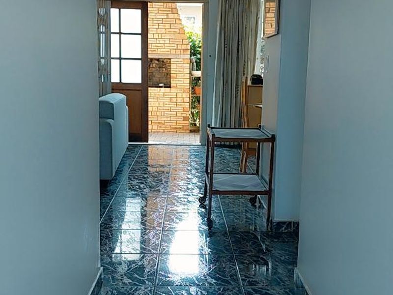 A bright hallway featuring polished blue marble-effect floor tiles, leading towards an exterior doorway with a view of a brick patio area.
