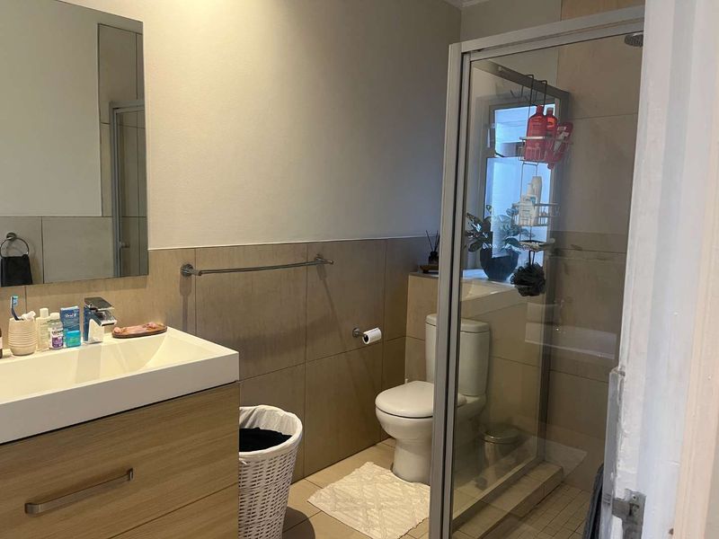 A modern bathroom featuring a vanity with basin, a glass-enclosed shower, and neutral wall tiling.