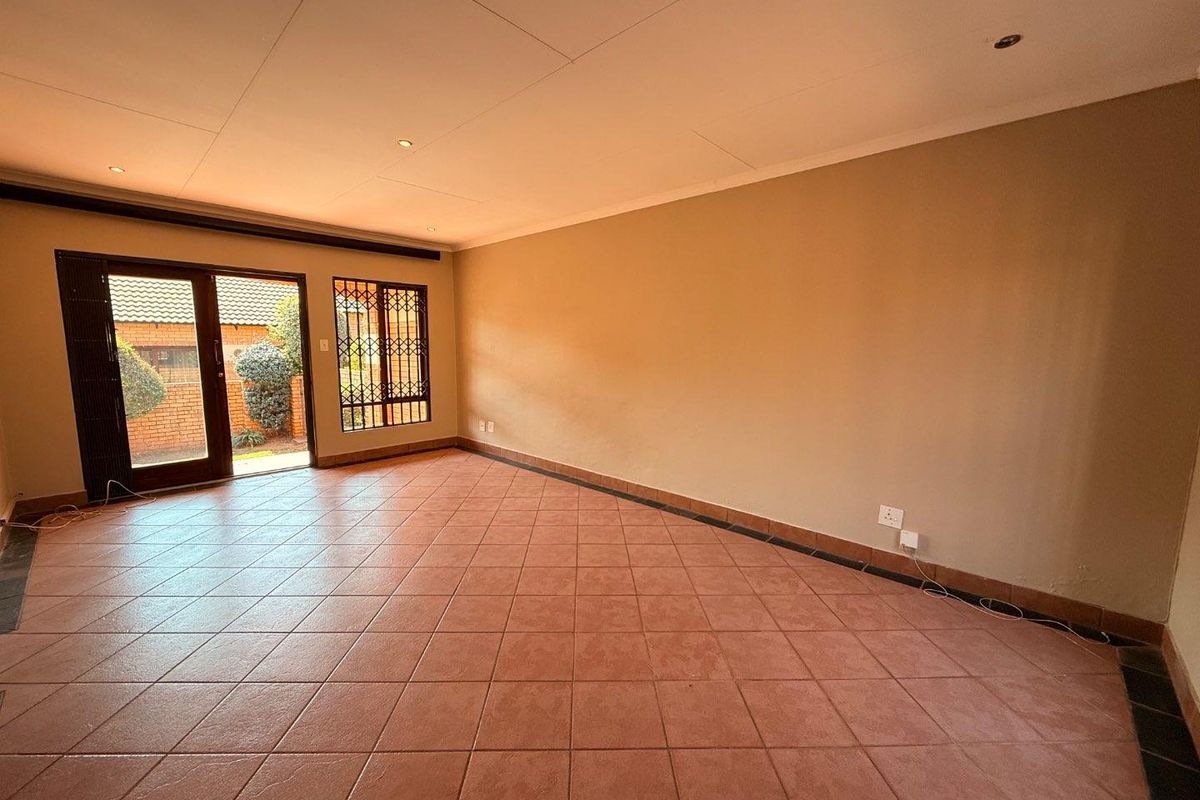 A spacious, empty living room featuring neutral walls, tiled flooring, recessed lighting, and direct access to an outdoor area through a sliding glass door.