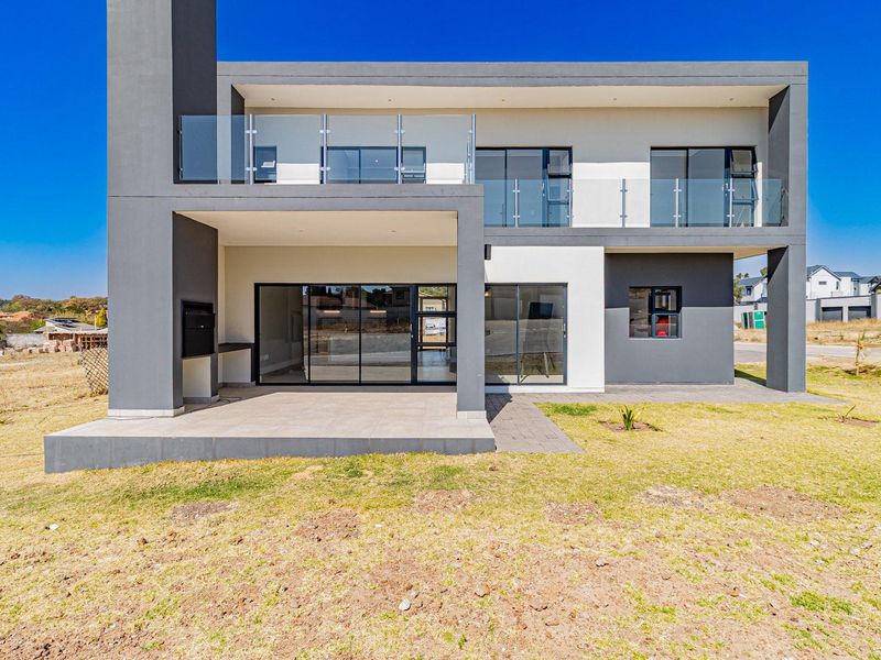 Modern double-storey residence featuring a covered patio with built-in braai, glass balustrades on the upper balcony, and large sliding doors for indoor-outdoor flow.