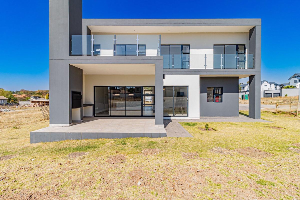Modern double-storey residence featuring a covered patio with built-in braai, glass balustrades on the upper balcony, and large sliding doors for indoor-outdoor flow.