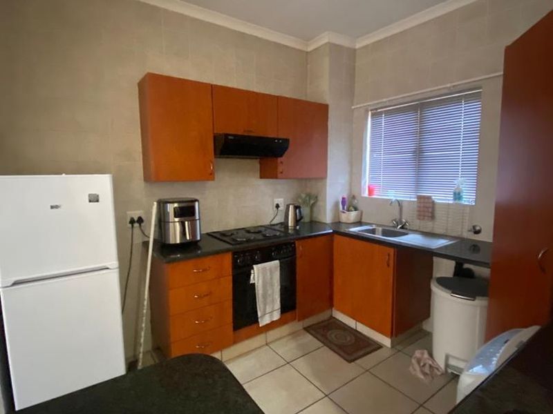 A functional kitchen featuring wooden cabinetry, dark countertops, built-in oven with gas hob, extractor fan, and tiled flooring.