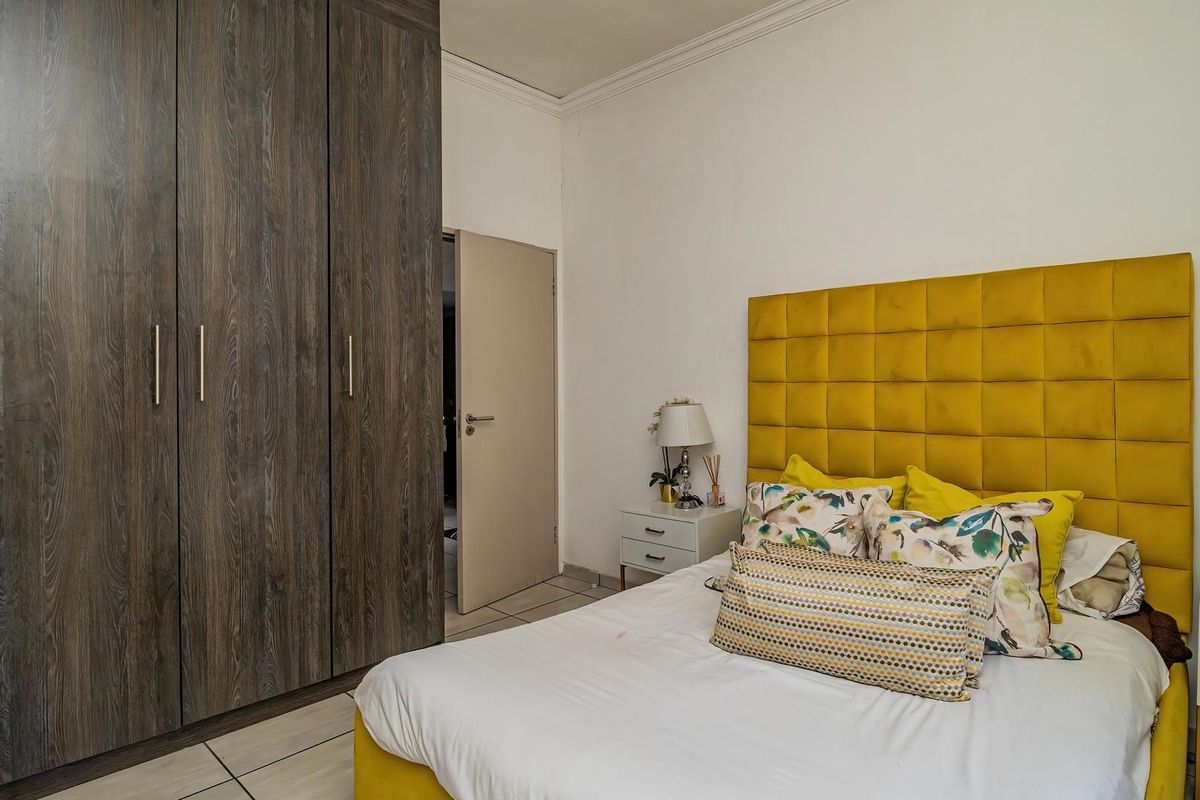 A well-maintained bedroom featuring dark wood-grain built-in cupboards, tiled flooring, and decorative ceiling cornicing.