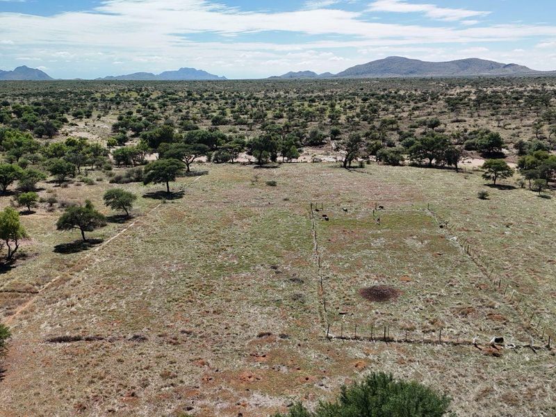 An aerial view of a large, open farm landscape featuring natural vegetation and sections of wire fencing.