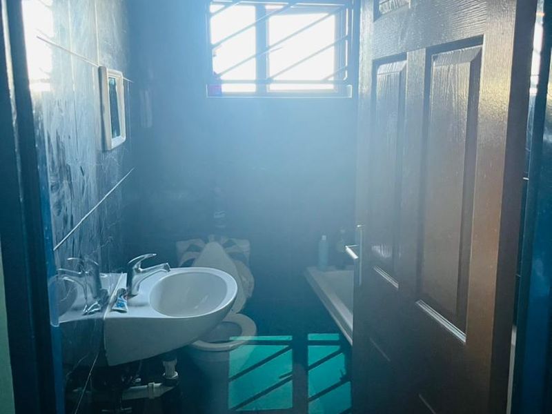 A compact bathroom featuring a wall-mounted basin, toilet, and tiled finishes, currently suffering from poor lighting and visibility.