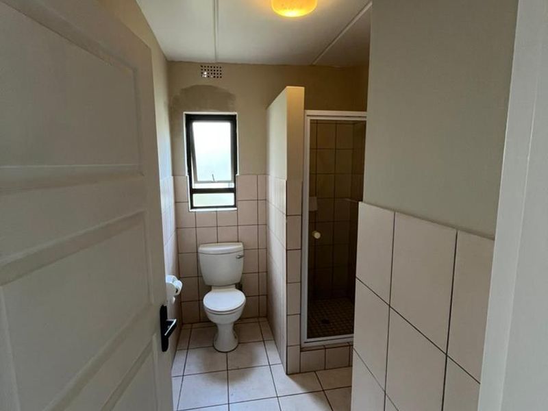 A functional bathroom featuring a toilet, a separate shower enclosure, and neutral tiled finishes throughout.