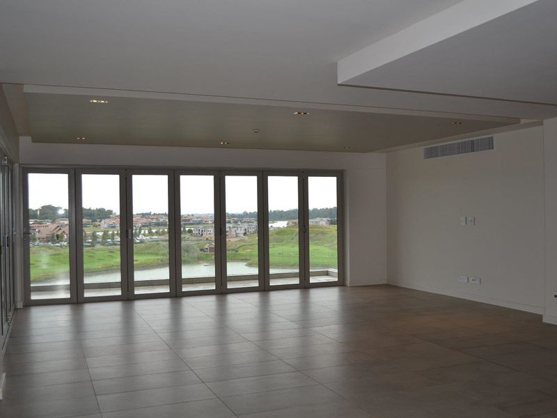 Spacious, empty living area featuring large bi-fold glass doors that open to a scenic golf course and water view, with modern tiled flooring.