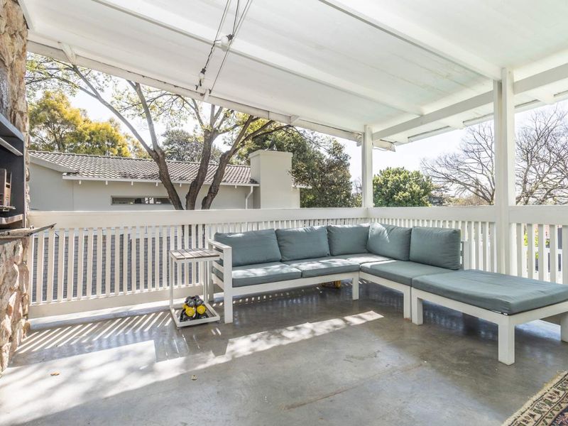 A covered patio featuring a built-in braai with stone cladding, white railing, and concrete flooring, offering a functional outdoor entertainment space.