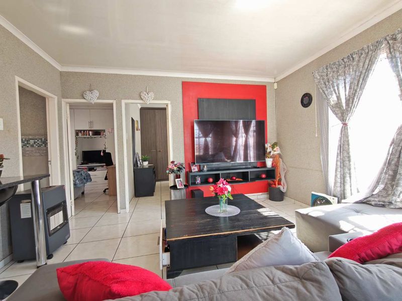 A living room featuring tiled flooring, a coved ceiling, and a prominent red accent media wall unit.
