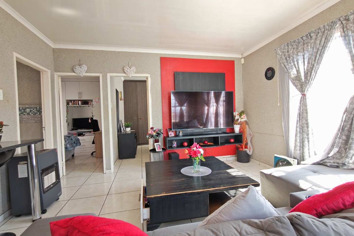 A living room featuring tiled flooring, a coved ceiling, and a prominent red accent media wall unit.