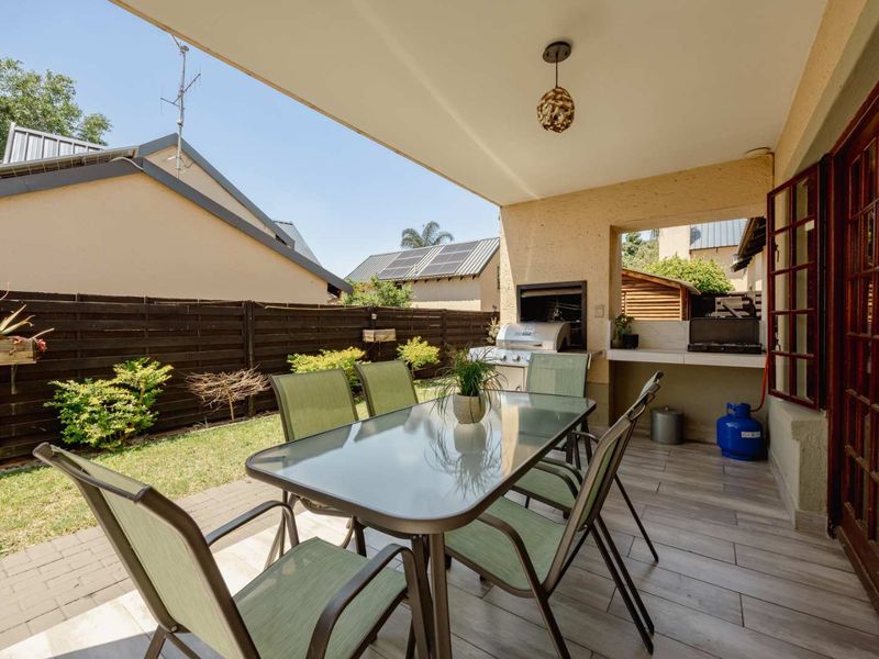 A covered patio area featuring a built-in braai, tiled flooring, and direct access to a private garden with timber fencing.