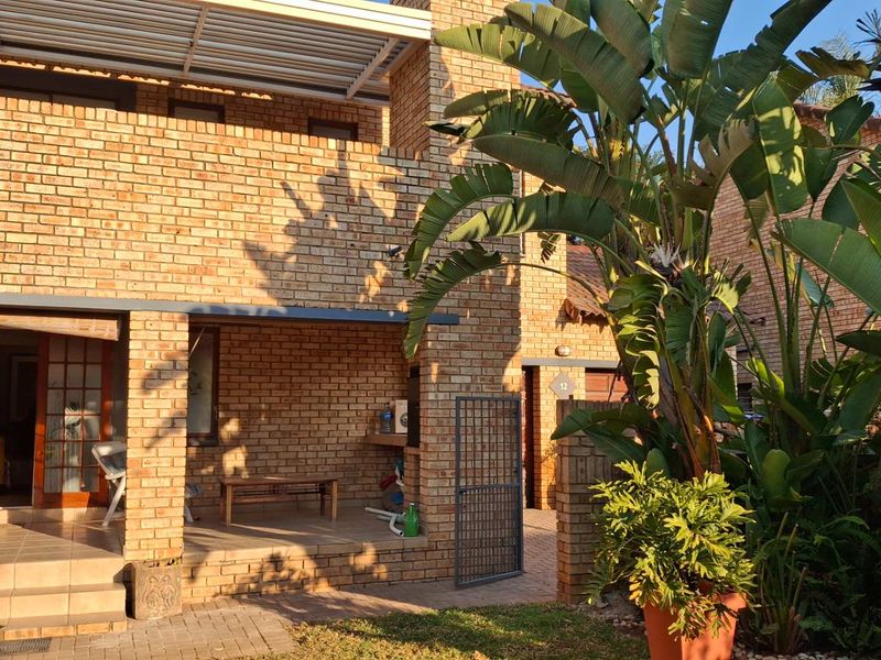 A rear view of the townhouse featuring a face brick facade, a covered patio area with a built-in braai, and a paved courtyard.