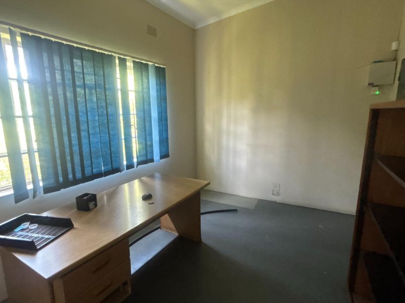 A functional office space featuring a large window with vertical blinds, neutral walls, and durable flooring, suitable for a professional workspace.