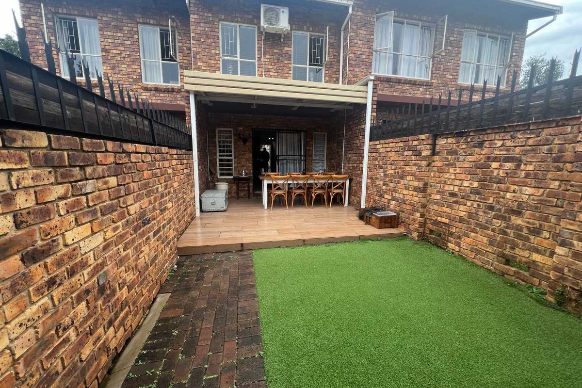 A private rear courtyard featuring a covered patio area, brick boundary walls, and a low-maintenance artificial lawn.