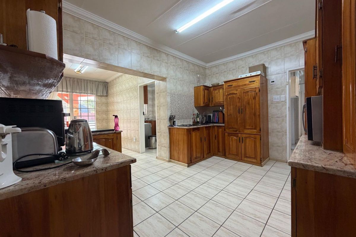 A functional kitchen featuring extensive wooden cabinetry, granite countertops, and tiled finishes throughout, offering a traditional layout with potential for modern updates.