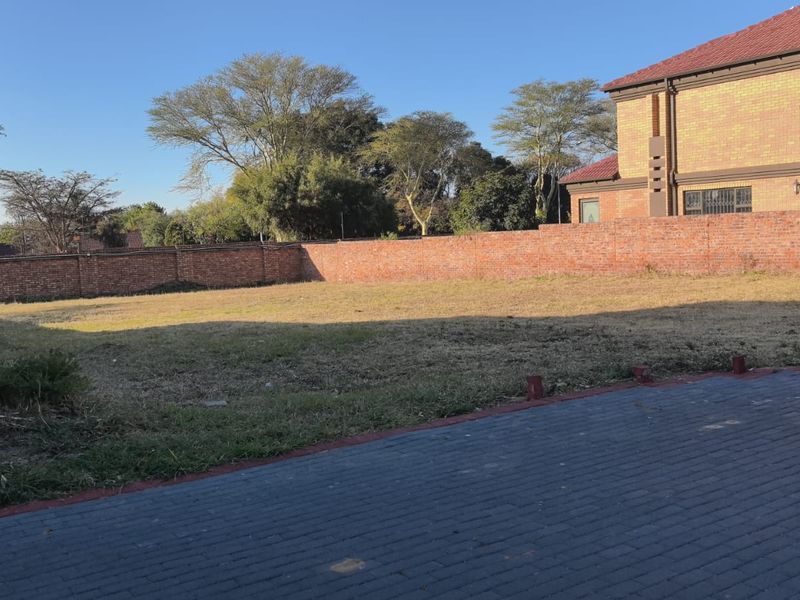 A vacant residential plot featuring a brick boundary wall and paved driveway access, offering a clear space for future development.