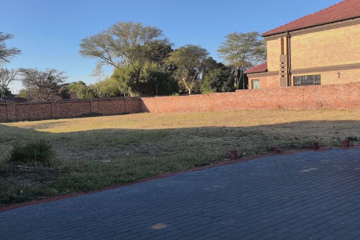 A vacant residential plot featuring a brick boundary wall and paved driveway access, offering a clear space for future development.