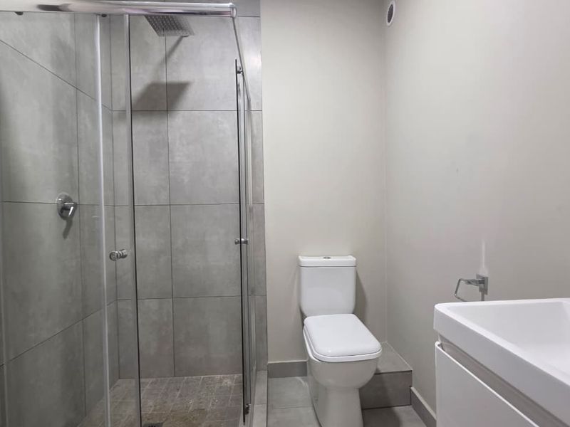 Modern bathroom featuring a walk-in shower with glass screen, rain shower head, contemporary toilet, and a sleek vanity basin with tiled finishes.