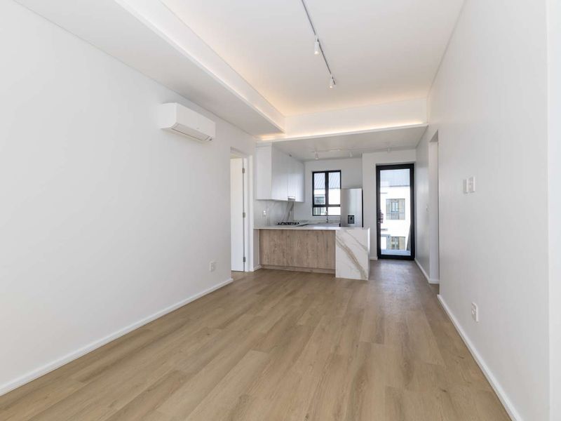 Modern open-plan living area featuring light wood-look flooring, a sleek kitchen with stone island, and integrated air conditioning in a bright, neutral space.
