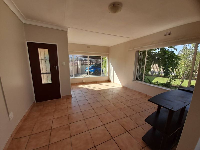 A bright, empty living area featuring tiled flooring, large windows with security bars, and direct access to the exterior.