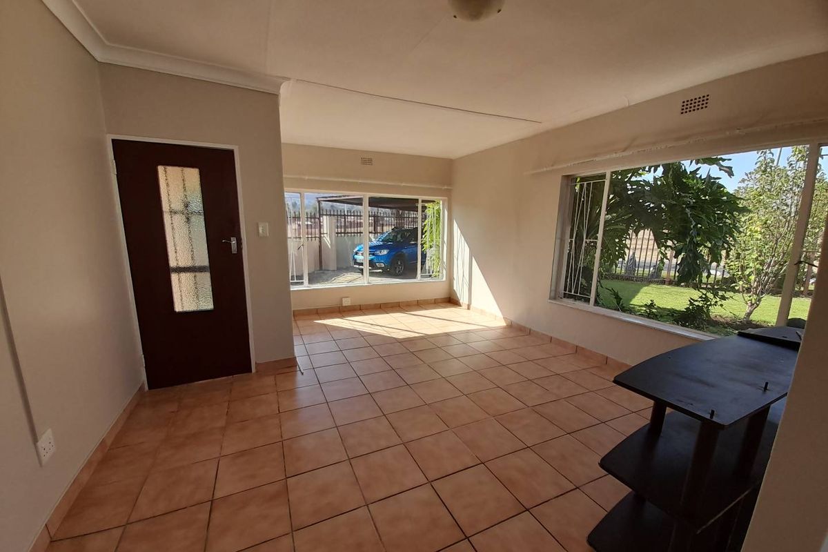 A bright, empty living area featuring tiled flooring, large windows with security bars, and direct access to the exterior.