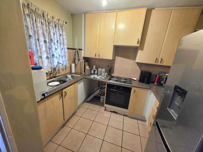 A compact kitchen featuring light wood-tone cabinetry, tiled flooring, and built-in cooking appliances, offering a functional layout with potential for modern cosmetic updates.