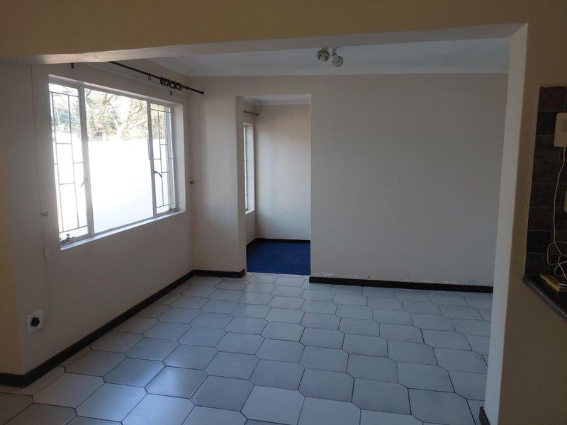 An empty living area featuring tiled flooring, neutral walls, and metal-framed windows, offering a blank canvas for potential interior design updates.