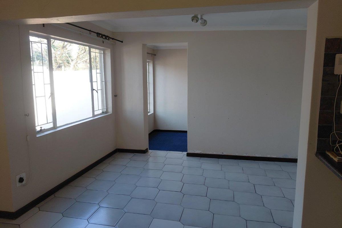 An empty living area featuring tiled flooring, neutral walls, and metal-framed windows, offering a blank canvas for potential interior design updates.