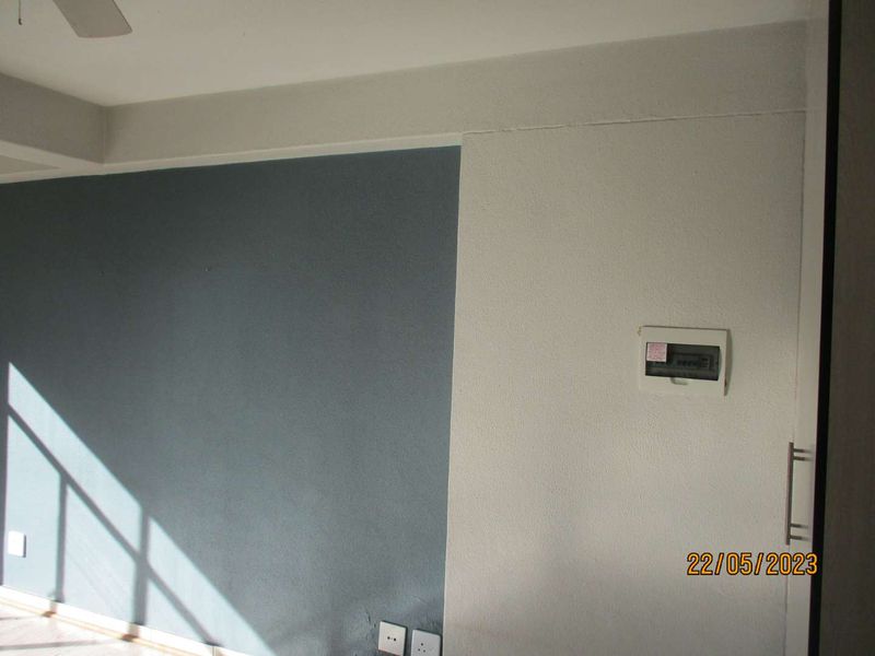An empty living area featuring a two-tone painted wall, an integrated electrical distribution board, and a ceiling fan.