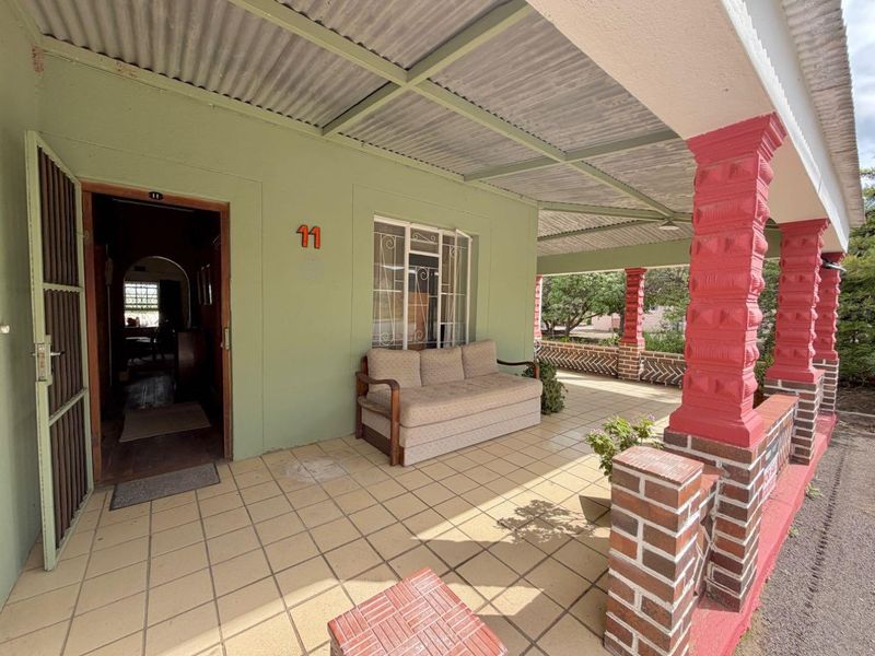 A covered patio area featuring tiled flooring, decorative brick columns, and a corrugated metal roof, providing a functional outdoor entrance space.