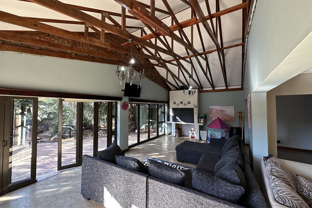 Spacious living room featuring high vaulted ceilings with exposed timber trusses, a built-in fireplace, and large aluminium stacker doors opening to the patio.