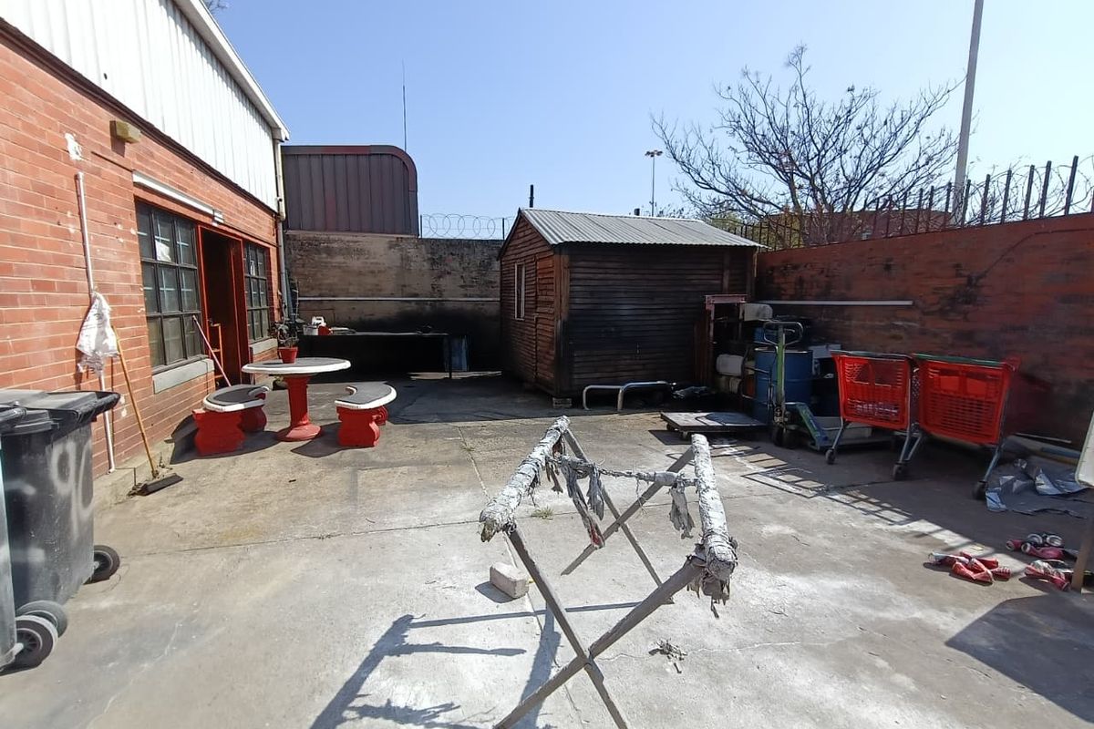 Rear industrial yard area featuring concrete paving, a timber storage shed, and enclosed brick boundary walls with security fencing.