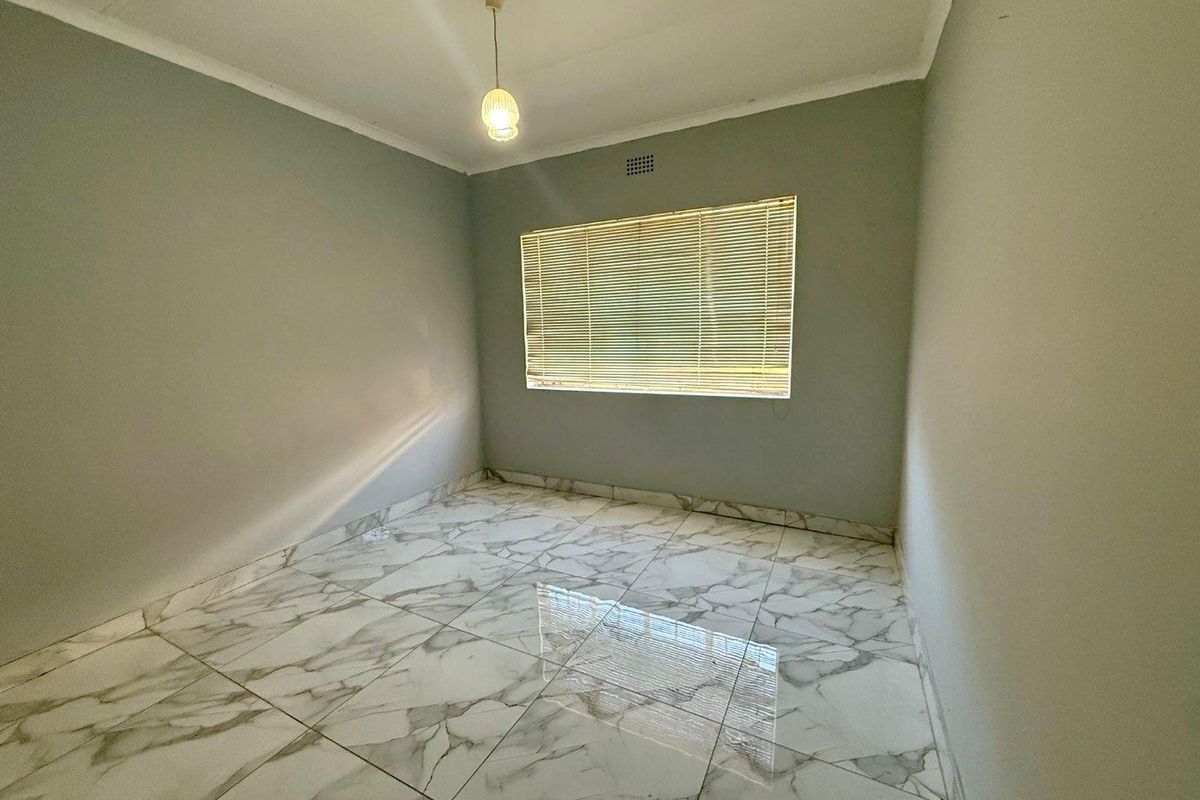 A clean, empty bedroom featuring modern marble-look floor tiles, neutral grey walls, and a fitted window blind.