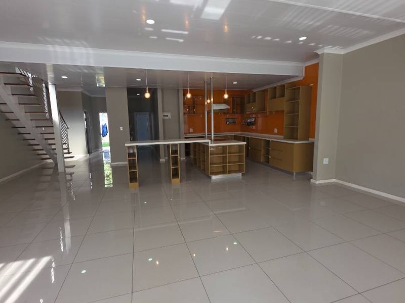 Spacious open-plan living area featuring a modern kitchen with island, tiled flooring, and a staircase leading to the upper level.