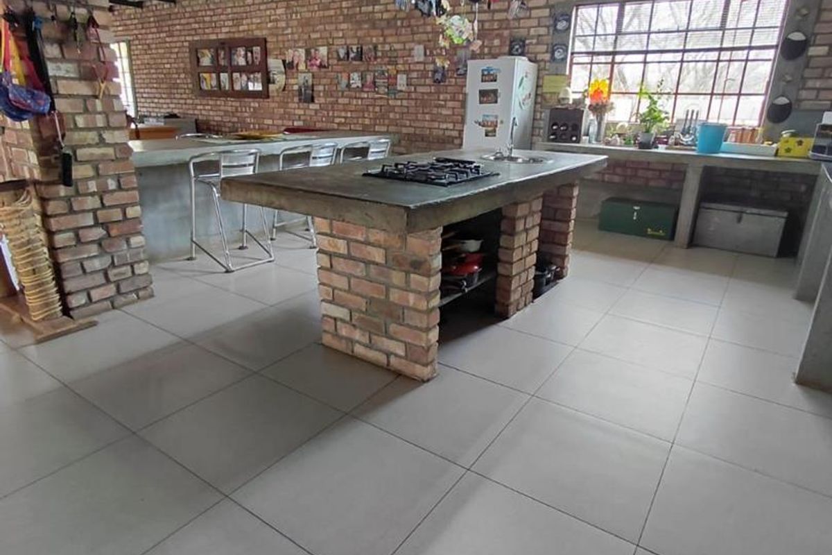 Spacious industrial-style kitchen featuring exposed brick walls, steel ceiling beams, a large concrete island with a built-in gas hob, and tiled flooring.